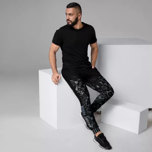Mann mit Designer Jogginghose Herren - Modell Baroque Ornaments von Antony Yorck - sitzt auf einem Podest und schaut dabei nach rechts, seine linke Hand steckt in der Hosentasche, sein rechtes Bein ist ausgestreckt und der Schriftzug ANTONY YORCK ist auf dem Galonstreifen zu erkennen. - Baroque Noir Collection