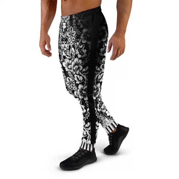 Ein Mann steht vor einem weißen Hintergrund und trägt eine schwarze Jogginghose der Marke ANTONY YORCK mit einem auffälligen weißen floralen Muster im baroque Noir Stil. Die Hose weist den Schriftzug "ANTONY YORCK" am Bein auf und hat ein gestreiftes Bündchen. Der Mann kombiniert sie mit schwarzen Sportschuhen. Perfekt für luxury urban street style, streetwear fashion, subversive style und hiphop style Liebhaber. Entdecken Sie mehr auf https://antonyyorck.com. Schlüsselwörter: trendy menswear, modern fashion, designer joggers, urban clothing, stylish activewear.