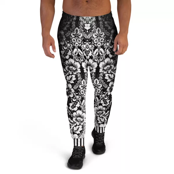 Ein Mann steht vor einem weißen Hintergrund und trägt eine schwarze Jogginghose der Marke ANTONY YORCK mit einem auffälligen weißen floralen Muster im baroque Noir Stil. Die Hose weist den Schriftzug "ANTONY YORCK" am Bein auf und hat ein gestreiftes Bündchen. Der Mann kombiniert sie mit schwarzen Sportschuhen. Perfekt für luxury urban street style, streetwear fashion, subversive style und hiphop style Liebhaber. Entdecken Sie mehr auf https://antonyyorck.com. Schlüsselwörter: trendy menswear, modern fashion, designer joggers, urban clothing, stylish activewear.